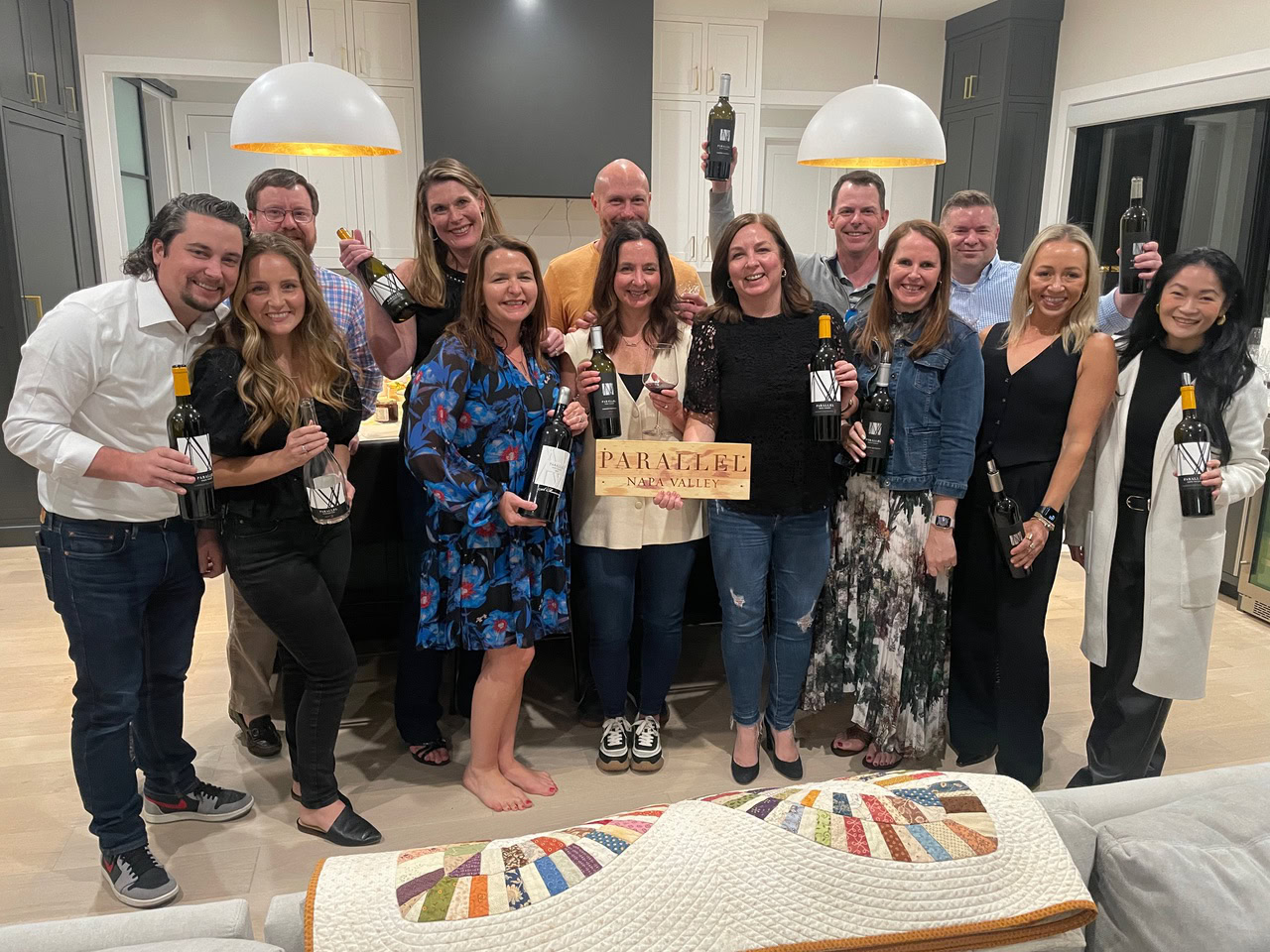 Group of people celebrating with bottles of Parallel Wines in a modern kitchen.